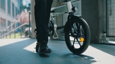 İş adamlarının ayaklarına yakın durun ve elektro aracı onun yanına taşıyın. Elektro bisikletiyle iş merkezinin yakınında bir erkek patron. İnsanlar, teknoloji, ulaşım konsepti