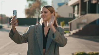 Başarılı genç iş kadını müşterileriyle dışarıda video görüşmesi yapmak için cep telefonu kullanıyor. Bayan, modern binanın yanında yürüyen yeni teknolojiyle konferans sohbeti yapıyor.
