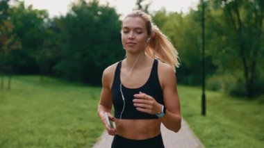 Kadın sporcu parkta spor kıyafetleri içinde koşuyor ve kulaklıkla müzik dinliyor. Müzikle çalışmak. Spor insanları konsepti