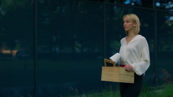 一个刚刚被释放的没有工作的金发女人 带着一个装有工作物品的盒子 走到工作的地方 悲伤地看着 她的侧面形象 失业人员的概念 — 图库视频影像