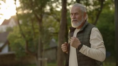 Olgun adam gün batımında akıllı saat takarak parkta koşuyor. Yaşlı bir erkek dışarı koşuyor. Kaçak. Spor ve sağlıklı yaşam tarzı kavramı. Genççe yaşlanmak