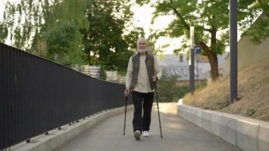 Gülümseyen kıdemli İskandinavyalı sokakta tek başına yürüyordu. Yaşlı erkek sporcu İskandinav yürüyüşü yapıyor. Genççe yaşlanıyor. Spor ve insanlar konsepti