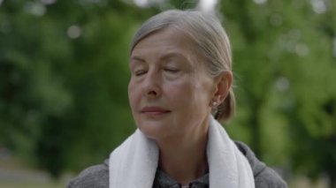 Parkta boynunda havluyla dikilen spor elbiseli gülümseyen olgun kadının portresini yakından çek. Kameraya bakan bir bayan sporcu. Genççe yaşlanmak