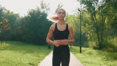 Parkta koşan, kulaklık takan, dışarıda antrenman yaparken müzik dinleyen bir bayan sporcu. Koşucu aktivitesi. Kardiyo egzersizleri. Egzersiz konsepti