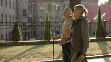 Yürüyüş sopalarıyla sokakta yürüyen mutlu, olgun bir çift. Birlikte Nordic yürüyüşü pratiği yapıyorduk. Genççe yaşlanıyor. Yaşlılar ve spor anlayışı