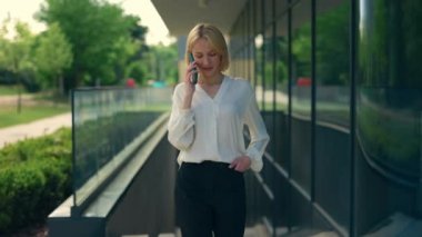 Resmi takım elbiseli mutlu iş kadını iş merkezinin yakınına gidip müşterilerle telefonda konuşuyor. Bayan yönetici dışarıda cep telefonuyla konuşuyor. İnsanlar ve mobil iletişim