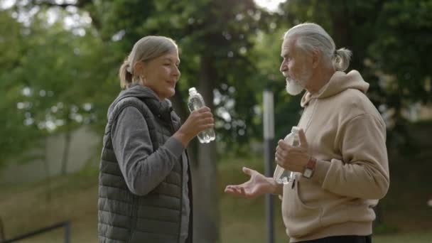 先輩の素敵な家族が話し合い 訓練後に水を飲んでいます 高齢者のカップルが一緒に公園で時間を過ごす 愛の関係の概念 — ストック動画