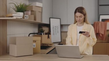 Young woman pays for purchases from a new apartment via the Internet using a card and a laptop at new home. Lady is paying online using laptop indoors in new house