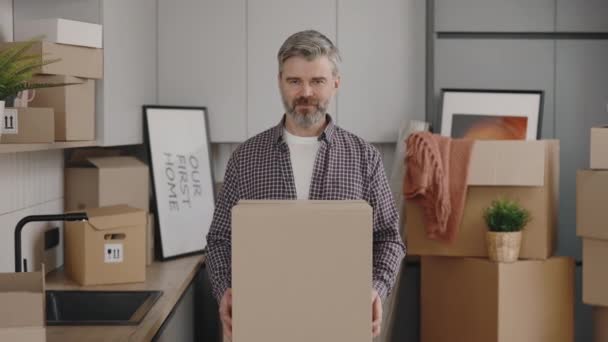一个快乐的男人手里拿着一个大盒子 在重新安置的过程中对着镜头的画像 微笑的男房客对搬进新公寓感到满意 新家和搬家的概念 — 图库视频影像