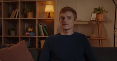 Young positive Guy with green eyes turning head and Looking to Camera. of caucasian handsome Male person posing while sitting on couch at Home. Man Portrait. Concept of emotions