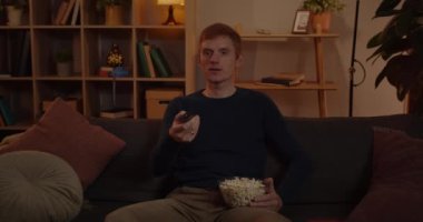 Kızıl saçlı adam uzaktan kumandayı alıyor ve televizyonu açıyor. Oturma odasında rahat bir şekilde oturup film izlerken patlamış mısırlı heyecanlı erkek tutucu kasesi.