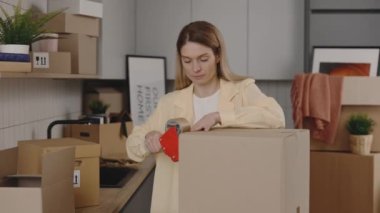 Woman Is Packing Home Things For Relocation. Middle Aged Woman Is Moving And Packing Dishes On The Kitchen Background. Moving People Concept