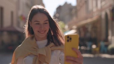Pretty Young Deaf Woman Having Video Chat Walking on Street and Gesturing with Fingers Phrase: Have You Heard the Latest News. Attractive Girl Having Video Call on Smartphone in Sign Language
