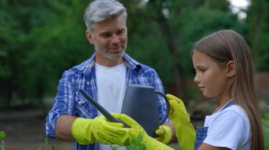 Farmer Teaching His Daughter How to Watering the Mint Plants from the Water Can. Male Worker Showing the Girl How to Use the Agro Tool. Family Small Business and Healthy Lifestyle