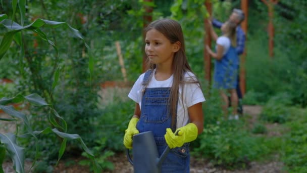 站在种植园里 拿着水罐的小农家女儿的画像 戴着农具 穿着特殊园艺服装 看相机的笑脸女孩 — 图库视频影像