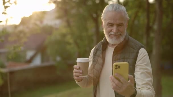 Veselý Serion Man Pomocí Smartphone Nesoucí Šálek Kávy Při Procházce — Stock video