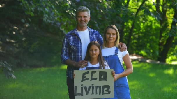 地球を救うための環境運動の手の中に保持するエコ活動家の家族 公園に立つ白人夫婦とその娘の肖像画 エコリビングポスターを保持します — ストック動画