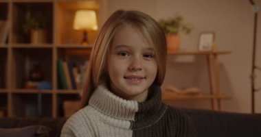 Oturma odasındaki koltukta oturan ve gülümseyen kameraya bakan sevimli genç kızın yakın çekimi. Evdeki Kanepede otururken Güzel Bayan Çocuk Poz Vermenin Portresi. Halk Portresi