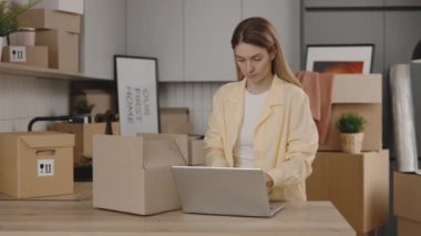 Genç Kafkas Kadın Laptop Kullanıyor ve Tüm Malların Arka planda Birçok Kutuyla Gelip Gelmediğini Kontrol Ediyor. Yeni Ev ve Taşınma Konsepti