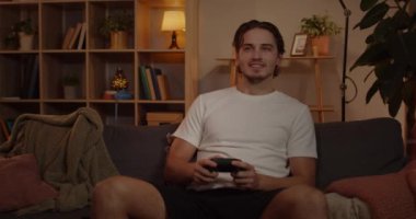 Video oyunu oynayan ve joystick kullanan heyecanlı beyaz adamın ön görüntüsü. Yakışıklı genç adam oturma odasında kanepede otururken yalnız zaman geçirmekten zevk alıyor. Boş zaman ve eğlence anlayışı