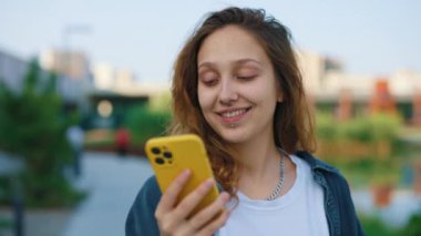 Güzel beyaz kadın dışarıda yürüyor, akıllı telefon kullanıyor, göl kenarına yakın duruyor, mesaj yazıyor, not yazıyor. Uygulama Cep Telefonu kullanan genç bir öğrenci. Yakın çekim. Halk ve Teknoloji Konsepti