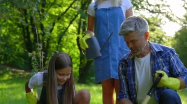Parktaki Genç Beyaz Aile Bitkileri Ağacı. Adam, Bayan Çocuğa Bahçıvanlığı öğretiyor. Toprakta Kürek ve Pad Bitkisi Olan Mutlu Aile. Halk ve Güvenli Ekoloji Konsepti