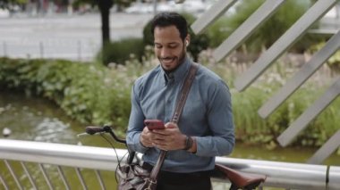 Mutlu Afro-Amerikan iş adamı, kablosuz kulaklıklarıyla sokakta bisikletin yanında oturmuş elinde modern akıllı telefonuyla uygulama iletişimi kullanarak mesaj yolluyor. İş yerinde başarı ve iyi haberler..