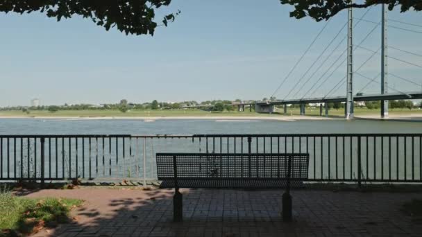 ドイツ デュッセルドルフ 2021年7月1日 背景に空のベンチ穏やかな水とライン橋の川の風景 晴れた夏の日 ドイツのデュッセルドルフ — ストック動画