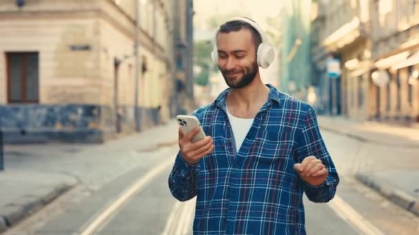 一个年轻的旅行者 戴着时髦的耳机 愉快地穿梭于古城中心 听着音乐和跳舞 他是一个享受生活的街头旅游者 音乐情人 — 图库视频影像