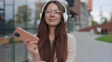 Kendine güvenen kadın yönetici cep telefonundan müzik dinliyor ve işten sonra dinleniyor. Heyecanlı Bayan Dans ve Şarkı Söyleyen Kulaklıklardan Müzik. Kulaklıklı Kadın Dans Ediyor