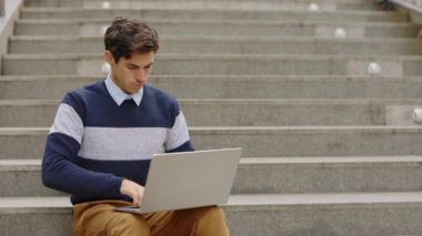 Dışarıda oturan yakışıklı yönetici, dizüstü bilgisayarda çalışıyor. İş adamı çalışıyor. Yabancı Öğrenci Bilgisayar Kullanarak Sokak Çalışması. Genç İşadamı merdivenlerde otururken dizüstü bilgisayar kullanıyor. Son teslim tarihi
