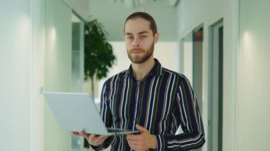 Ofiste elinde dijital dizüstü bilgisayarla duran kendine güvenen genç bir yöneticinin portresi. Bu başarılı serbest çalışan, ofis çalışanı ve kameraya bakan girişimci.