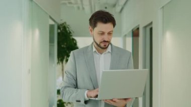 Yakışıklı İşçi, Girişimci, Ofiste Duran, Klavyede Dizüstü Bilgisayarı Tutan ve Yoğun Modern Ofiste Kameraya Gülümseyen. Tasarım, Veri Analizi, Planlama Stratejisi Üzerinde Çalışıyor.