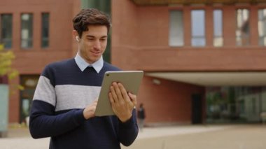 Yakışıklı İşadamı, Tablet Bilgisayarını kullanarak Ofis Yakınındayken Kaydırma, Tıklama ve Mesajlaşma. Gülümsüyor. Mutlu hissediyorum. Açık hava güneş ışığı. Yavaş Hareket.