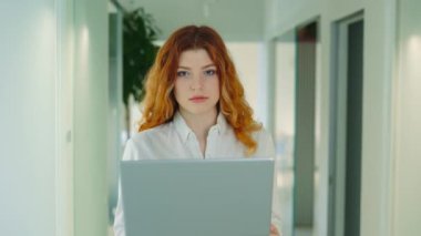 Ofis bilgisayarında kameraya bakan genç kızıl saçlı iş kadını portresi. İş yerindeki arkadaş canlısı bayan yönetici. Bilgisayar Yöneticisi Gülümseyen Portre Öngörünümü üzerinde çalışıyor