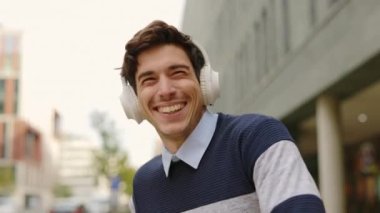 Kablosuz kulaklıklı mutlu iş adamı dışarıda ofis binasının yanında müzik ve dans dinliyor. Pozitif Erkek Girişimci Müzikten Hoşlanıyor, Başarılı Anlaşmayı Kutla