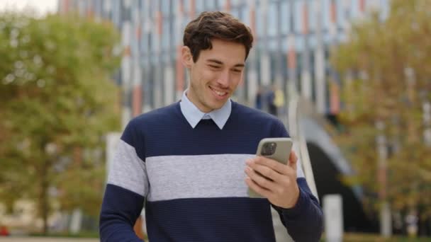 スマートフォン スクロールアプリ ワークチャートを使用した白人ハッピーマン 友人オンラインでテキスト ストリートに立っている携帯電話と外のガイオフィスワーカー — ストック動画