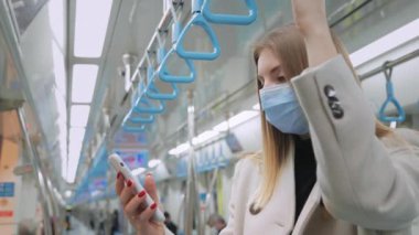 Tıbbi Koruyucu Yüz Maskeli Kadın Metroda Duruyor ve Smartphone kullanarak Mesaj Yazıyor. Koronavirüs salgını. Yeraltındaki Ekran Akıllı Telefonuna Bakan Kadın