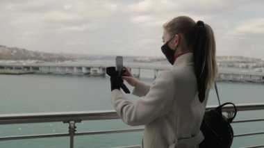 Gezgin Kadın Koruyucu Maske Takıyor, Pandemia 'yı izlerken Köprü' nün dışında video çekiyor. Karantina sırasında seyahat. Covid Kavramından Sonra Turist