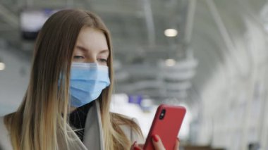 Tıbbi Yüzü Maskeli Kadın Havalimanında Salgın sırasında Cihazı Kullanıyor. Mesafe çalışması, mesajlaşma, kaydırma uygulamaları. Covid 'den sonra Airdrome' da telefonlu bir kadın yolcu. Turist