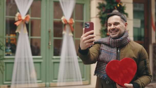 バレンタインデーに 妻への赤い形の贈り物を 両親に電話するビデオです スマートフォンを使用して幸せな男性 人と技術 クリスマス — ストック動画