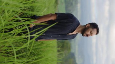 Dikey video. Dağlarda Uzun Çimlerde Duran Olumlu Adam 'ın Portresi, Yaşamı Düşünmek, Hayal kurmak. Turizm ve Seyahat Konsepti