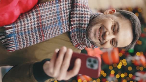 バーティカルビデオ スマートフォンを使ってバレンティーノのハート形の贈り物を保持する通りを歩くハンサムな男 外で笑った男 赤いクリスマスプレゼントテキスト スクロール — ストック動画