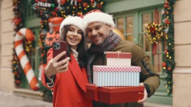 Güzel dekore edilmiş Noel sokağında dururken telefonda selfie çeken neşeli evli çift. Kış Tatillerinde Hafıza için Harika Arkadaşlar Fotoğraf Çekiyor. Şenlik Sezonu