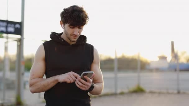 英俊的胡子运动员站在外面 用智能手机翻阅健身服进行体育锻炼 户外运动 健康生活方式及科技概念 — 图库视频影像