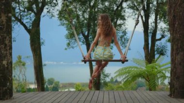 Zarif Uzun Saçlı Beyaz Kız Oturuyor, Dışarıda Sallanan Poz veriyor ve Bali 'de Güzel Manzarası var. Genç bayan dışarıda salıncakla eğleniyor. Seyahat ve Turizm Konsepti