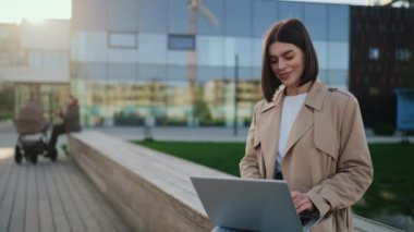 Güzel İş Kadını Uzaktan Çalışmak İçin Laptop Kullanıyor. Ofisin yanındaki bankta oturan genç bayan ve online çalışan. Halk ve Teknoloji Konsepti