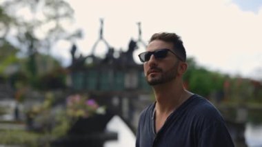 Dışarıda yürüyen iş adamı, tapınağın arka planında güneş gözlüğü takıyor. Çok Irkçı Adam Hedefe Gidiyor, Etrafa Bakınıyor. Turizm ve Seyahat Konsepti