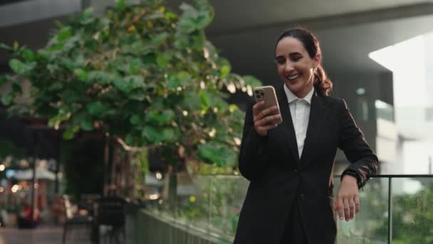 迷人的年轻女商人站在外面在电话荧幕上看有趣的新闻 迷人的女经理在智能手机上看滑稽视频和在户外大笑 — 图库视频影像