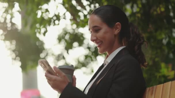 坐在长椅上和喝咖啡时 独自工作的女孩的侧视图 使用手机 上网浏览 迷人的正面经理 人与技术概念 — 图库视频影像